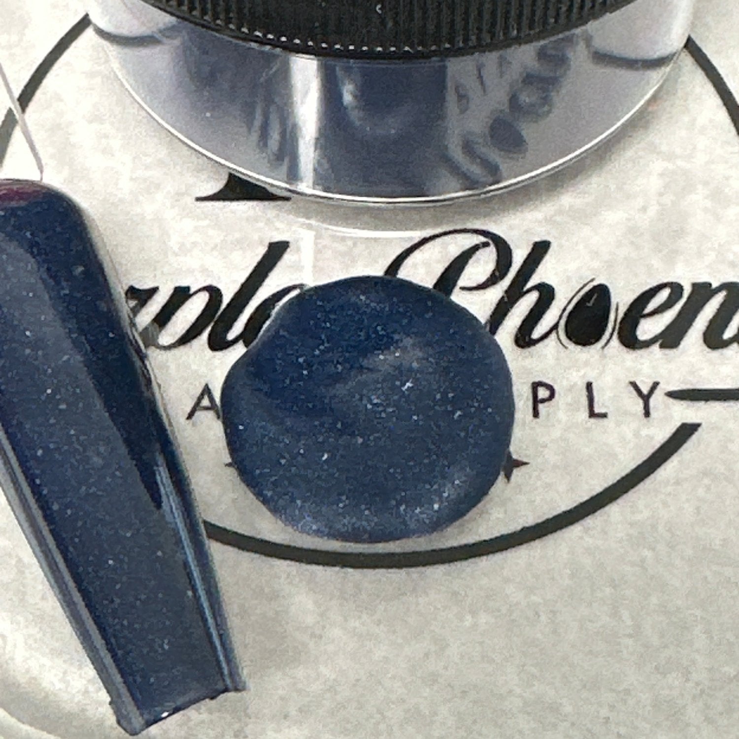 Close-up of Celestial Twilight Acrylic Powder - dark blue with shimmering gold flecks, applied on a nail tip, highlighting its luxurious, celestial appearance