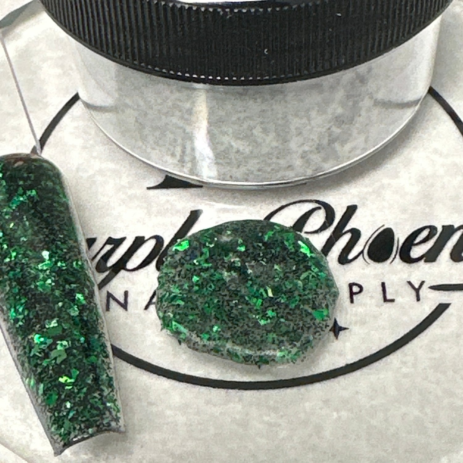 Swatch of Witch’s Brew Acrylic Powder - a deep green shade with iridescent glitter, applied on a nail tip, showcasing its enchanting, mystical finish